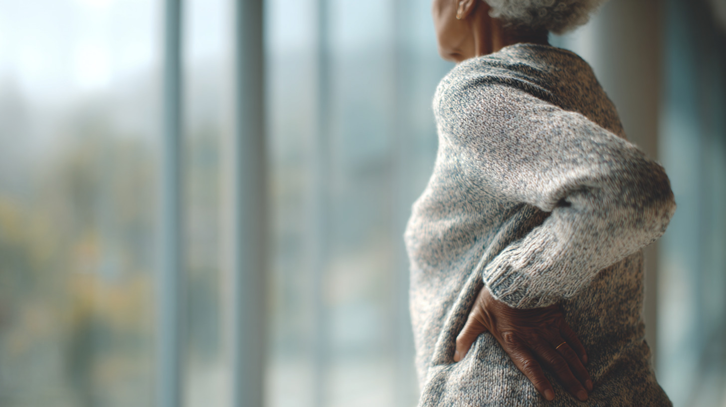 Personne âgée debout, main posée sur le bas du dos, illustrant les adaptations du corps au vieillissement.